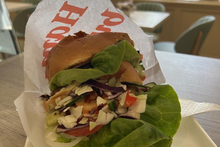 Friss salátával megpakolt hamburger papírban, a cukrászda asztalán