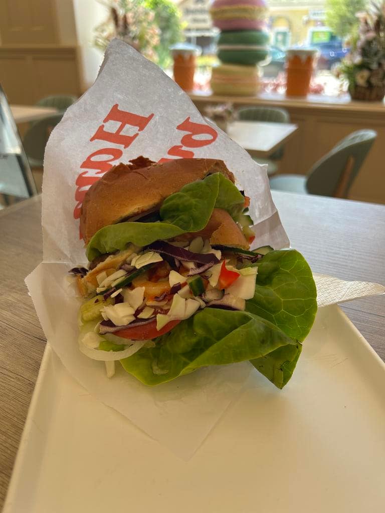 Friss salátával megpakolt hamburger papírban, a cukrászda asztalán